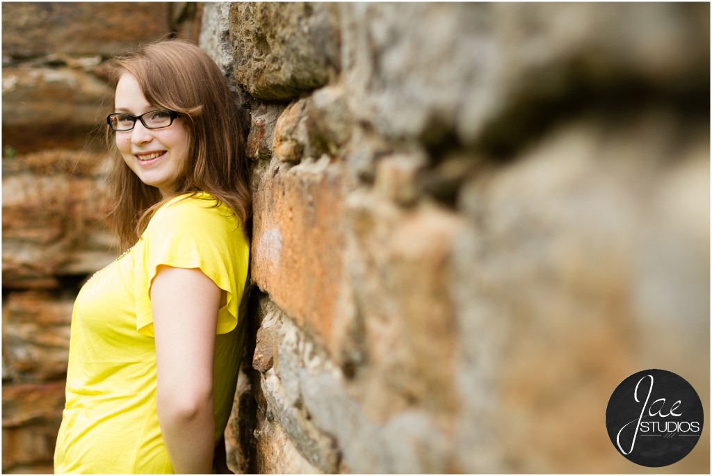 Lynchburg Senior Girl Emily 2014. She is reclined against the stone wall while smiling at the camera.