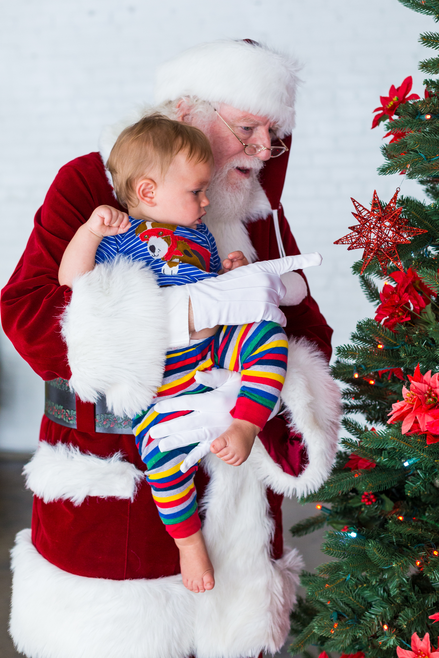 Santa holding an infant up to a Christmas tree